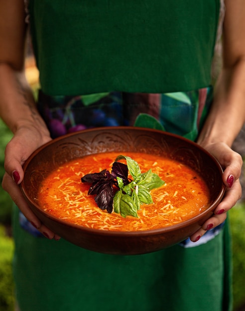 Woman is holding an earthen bowl with tomato cream soup.