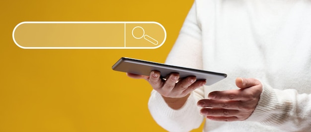 A woman is holding an electronic tablet on a yellow background Search for information on the Internet free access to the network