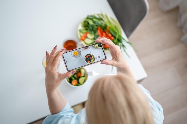 Photo a woman is holding a smartphone and capturing a photo of a nutritious breakfast spread