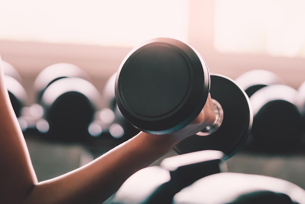 Woman is holding weight to train her arm and shoulder muscles in fitness gym