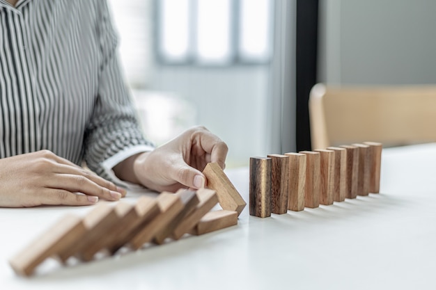 A woman is holding wooden blocks in a row, she grabs the center piece to complete them, the wooden block arrangement conveys the business operation by efficient management. Business idea.