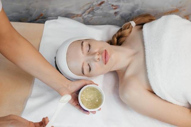 A woman is laying in a spa treatment with a mask on her head and a woman is getting a facial treatment.