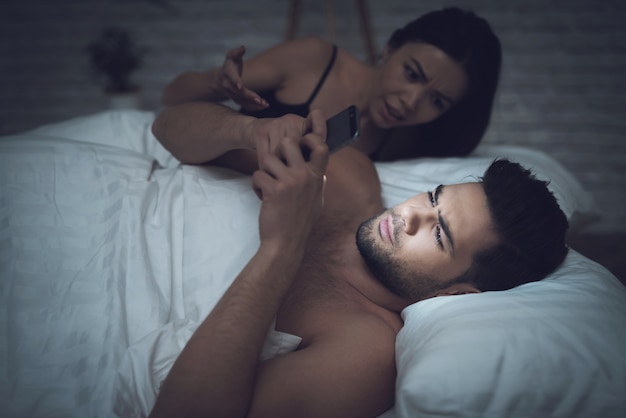 Woman is lying in dark room in bed with guy.