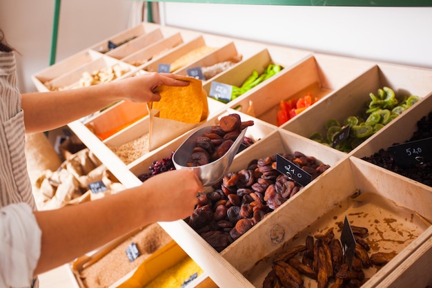 Woman is packing dried aprisots in the grocery shop. Dried fruits in the wooden boxes, vegan food