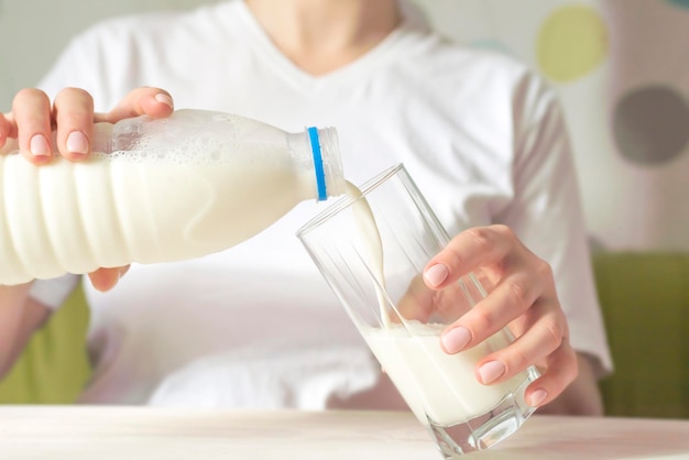 A woman is pouring milk from bottle in glass sitting at the table in kitchen