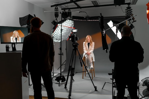 A woman is seated on a stool in a studio facing a camera the setting is an art event with visual