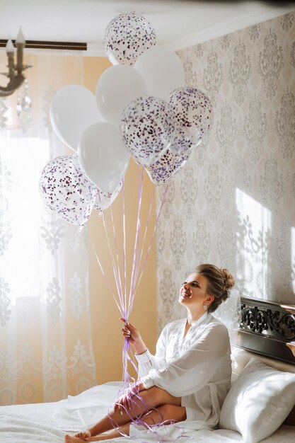 Photo a woman is sitting on a bed holding a bunch of balloons