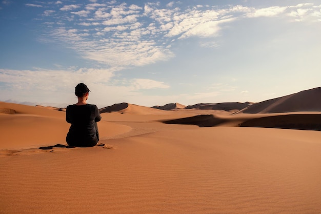 A woman is sitting on the golden sand dune of the Namib desert. Africa