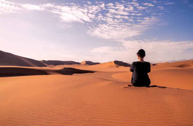 A woman is sitting on the golden sand dune of the Namib desert