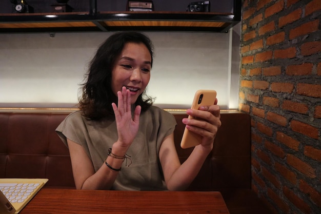 A woman is sitting at a table and is holding a phone with her hand up to her face.