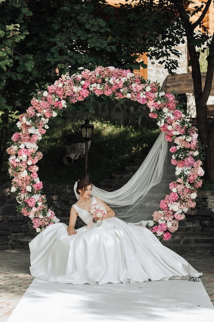 Photo a woman is sitting in a white dress in front of a pink arch