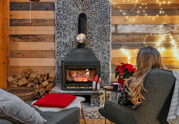 Woman is sitting with a cup of hot drink and a book near the fireplace