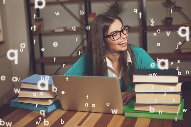 Woman is smilling She is working with lots of books and laptop at the wood table