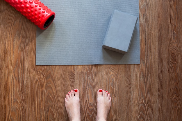 Woman is standing barefoot on floor in front of gymnastic mat and roller