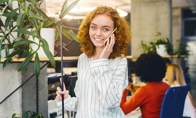 Photo a woman is standing in an office engaged in a phone conversation she is focusing on her call with