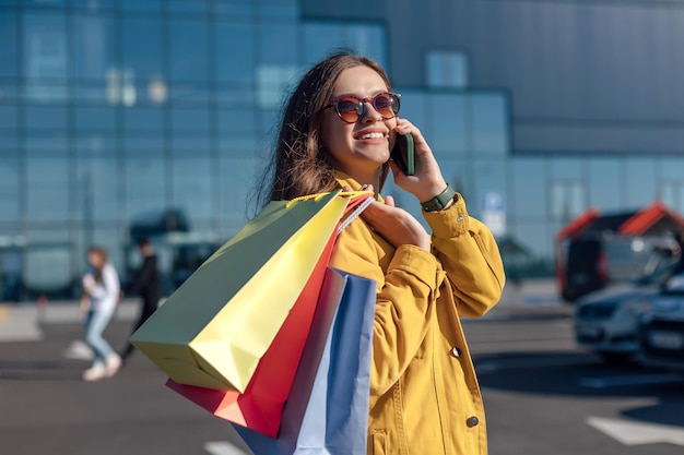 A woman is talking on the phone and holding bags on her shoulder