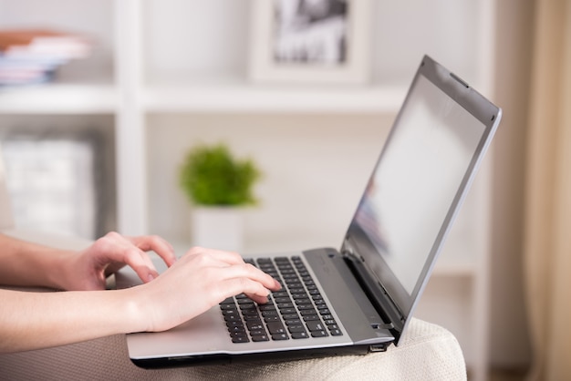 Woman is using laptop while sitting on couch at home.