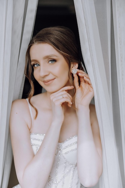 A woman is wearing a white dress and is putting on earrings