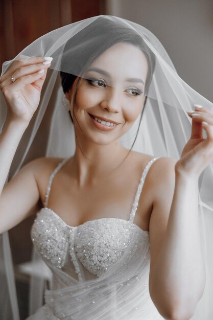 A woman is wearing a white wedding dress and holding a veil over her face