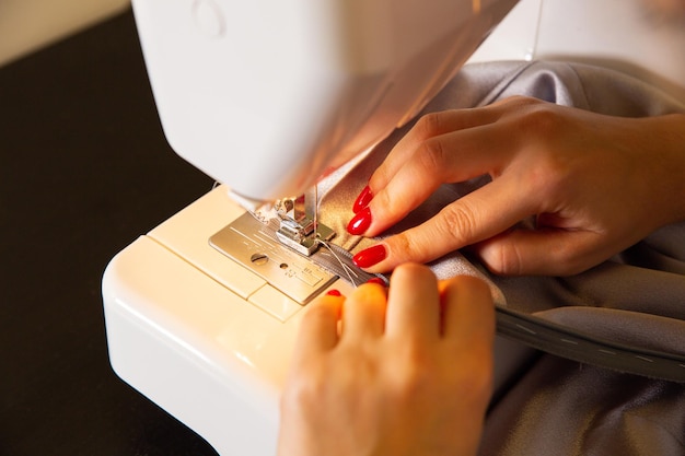 Woman is working at sewing machine Girls hands with red manicure Fashion concept Creating of new clothes process Hobby ideas