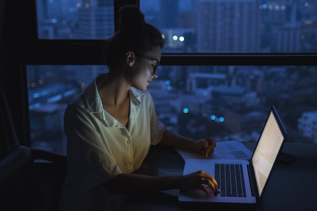 Woman is working with laptop at home during night.