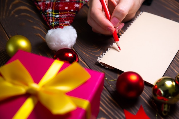 Woman is writing Christmas postcards. Greetings with holidays. Happy new year time. Congratulations to friends and family. Decorations on wooden table. Cozy mood. Copy space place.