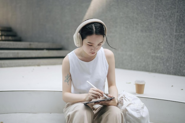 a woman is writing in a notebook and she is wearing a white tank top