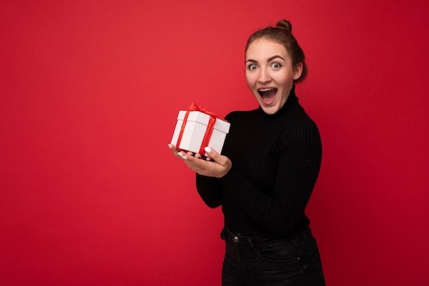 woman isolated over colourful wall wearing trendy outfit look holding gift box