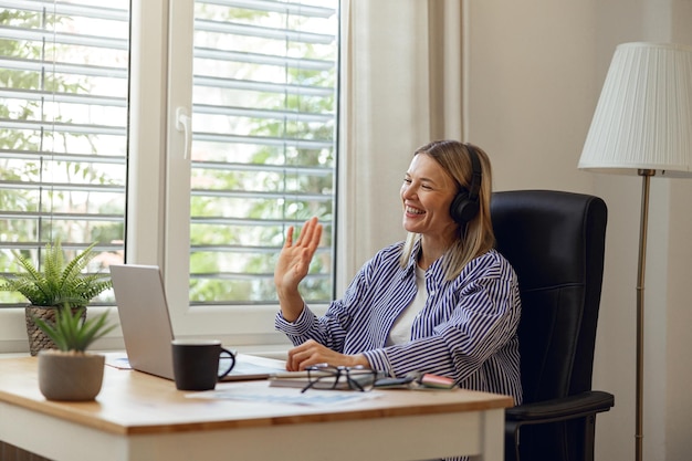 Woman it specialist talking waving hi to colleagues via video link during working from home office