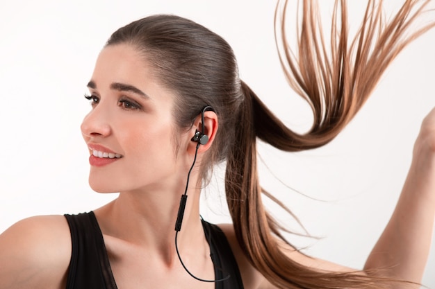 woman in jogging black top listening to music on earphones posing isolated on white