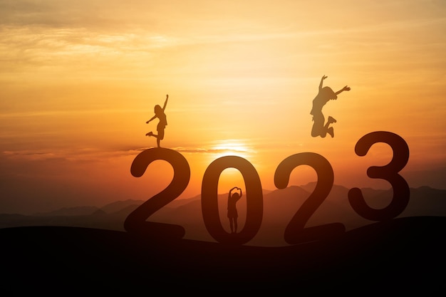 Woman jump happy new year 2023 concept silhouette of woman jumping over barrier cliff and success with beautiful sunset background Happy New Year 2023 use for web banner and advertisement