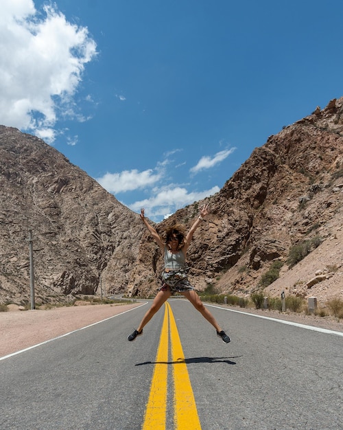 Woman jumping for joy on empty road with mountains