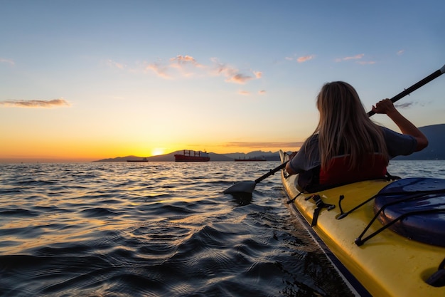 Woman on a kayak is paddeling in the ocean during a vibrant sunset