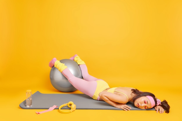 woman keeps hands on fitness ball feels very tired after weary training dressed in activewear lies on karemat 