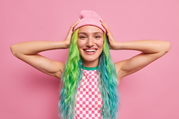  woman keeps hands to head happy to buy new outfit has dyes colorful hair has piercing in nose isolated on pink 