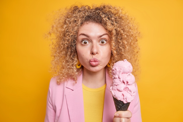 Photo woman keeps lips rounded looks surprisingly holds big strawberry ice cream has sweet tooth treats herself with delicious appetizing summer dessert