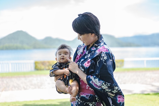 A woman in a kimono holds a baby in front of a lake