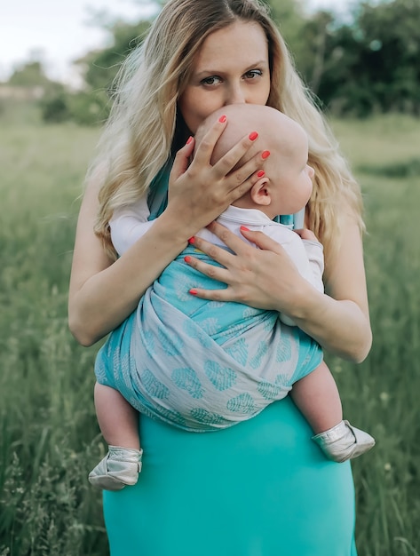 Woman kiss head of toddler child in sling carrier outdoors