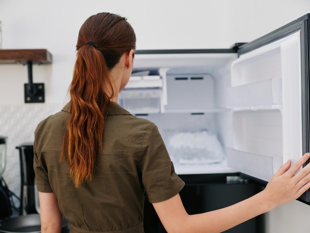 Photo a woman in the kitchen of her home opened an empty freezer with ice inside home refrigerator