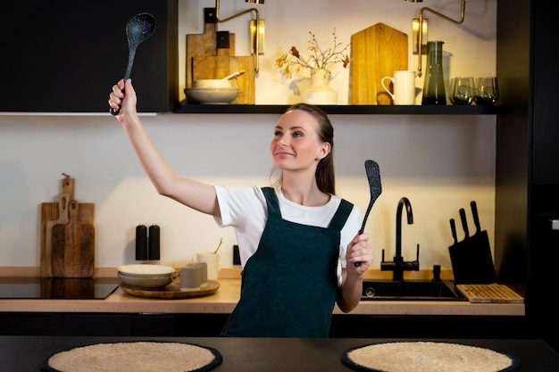 A woman in a kitchen holding a spatula and a kitchen utensil.