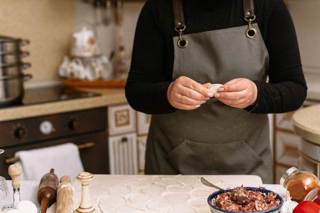 A woman in the kitchen sculpts homemade dumplings or semi-finished products. The cook wraps the minced meat from beef into the dough