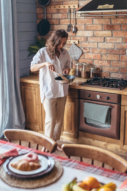 Woman in the kitchen at the stove stirring food in a frying pan