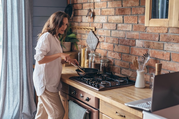 Woman in the kitchen at the stove stirring food in a frying pan