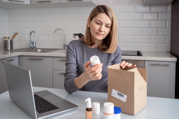 A woman in the kitchen with a laptop on the table She opens a box of dietary supplements Ordering food additives via the Internet