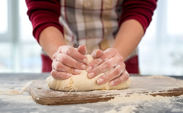 Woman kneading dough on wooden board for homemade pizza baking