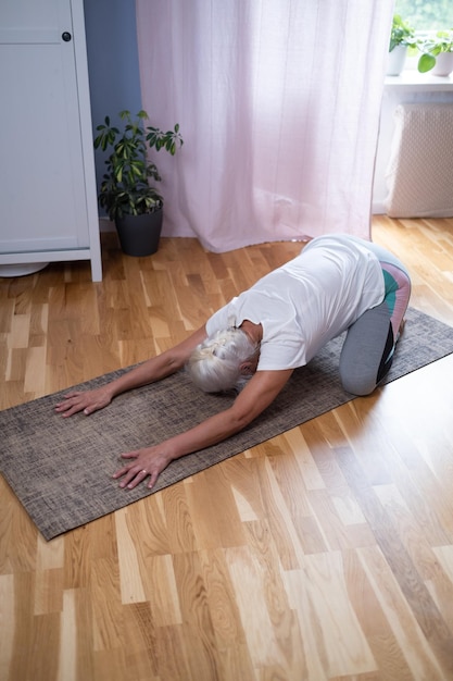 Woman kneeling on a mat and doing a balasana asana while practicing yoga at home