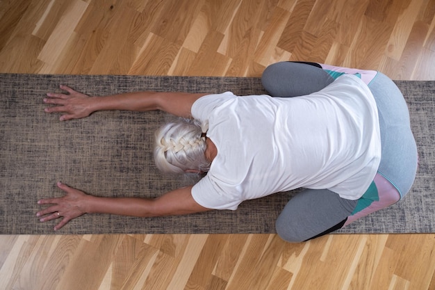 Woman kneeling on a mat and doing a balasana asana while practicing yoga at home