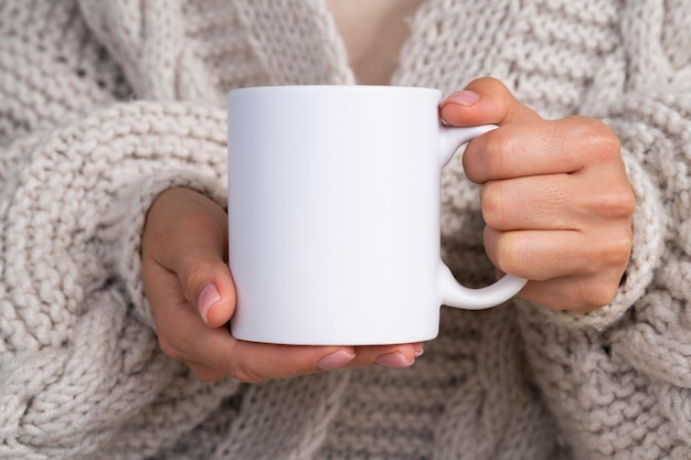 Woman in knitted sweater holding white mug in hands winter cup mockup for christmas individual gifts