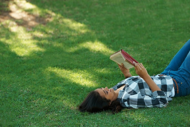 Woman knowledge and reading book on grass literature and smiling for fiction or fantasy story Female person nature and relaxing on lawn for education information and student studying in garden