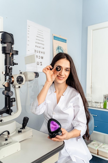 A woman in a lab coat holds a microscope and looks at a monitor.